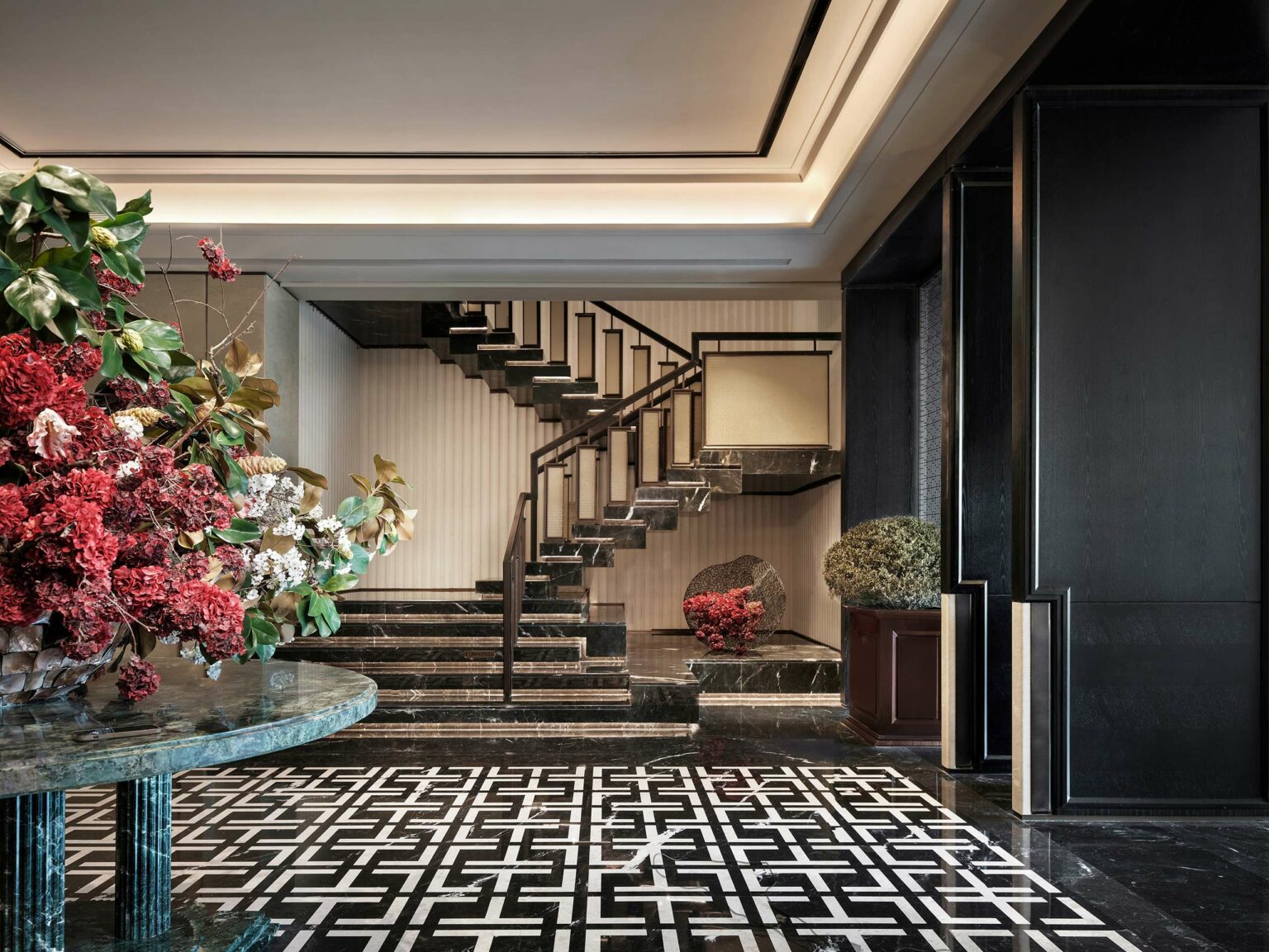Luxurious interior with a modern, floating staircase. Marble flooring with geometric patterns, elegant floral arrangement, and soft lighting create a sophisticated atmosphere.
