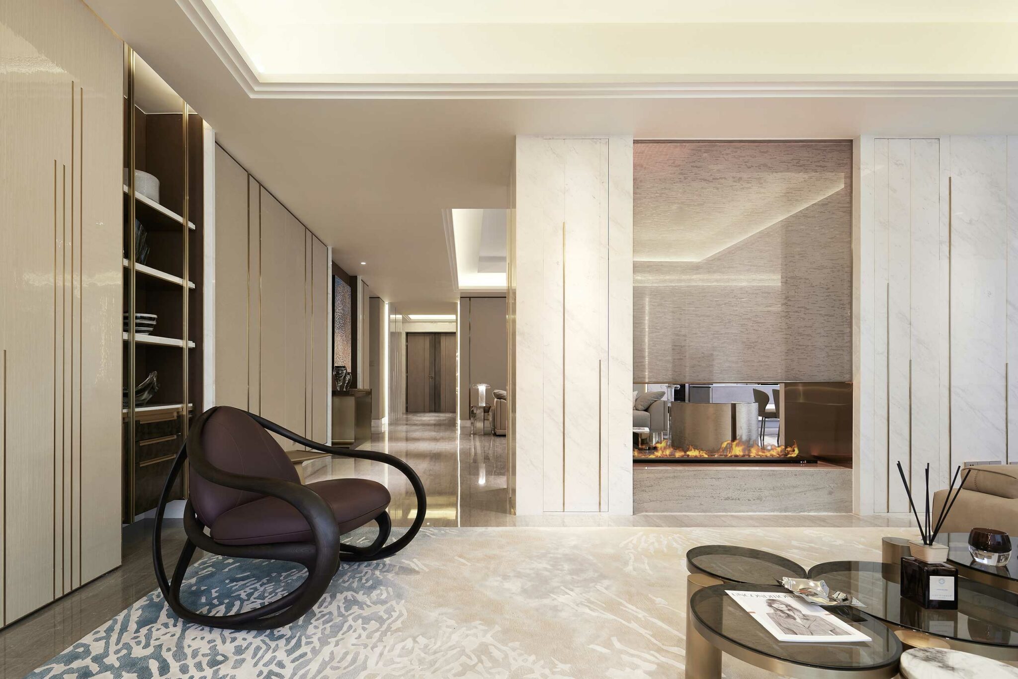 Luxurious living room with marble walls, modern fireplace, and sleek furniture. Features a curved black chair, glass tables, and warm ambient lighting.