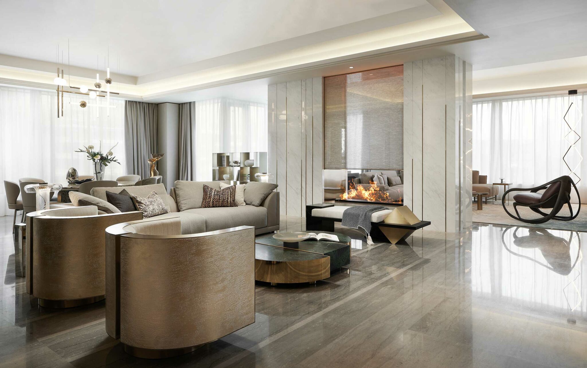 Elegant living room with sleek marble floors, modern beige furniture, and a cozy fireplace. Soft lighting and large windows create a warm, inviting ambiance.
