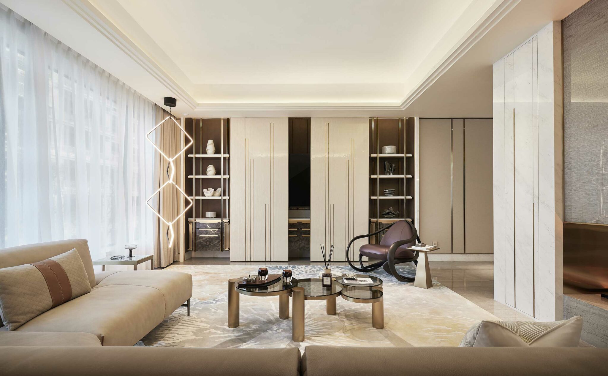 Luxurious modern living room with beige sofas, circular coffee tables, and geometric light fixture. Neutral tones and soft lighting create an elegant, serene atmosphere.