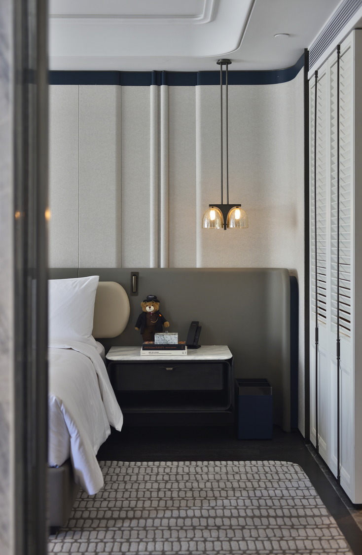 Modern hotel room with two beds, sleek gray tones, and elegant lighting. Features include a seating area, TV, and minibar, creating a cozy yet sophisticated ambiance.
