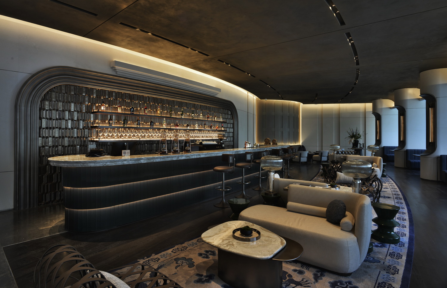 Luxurious hotel lounge with elegant furniture, soft lighting, and a marble bar. The modern design features curved architecture, plush seating, and warm tones.
