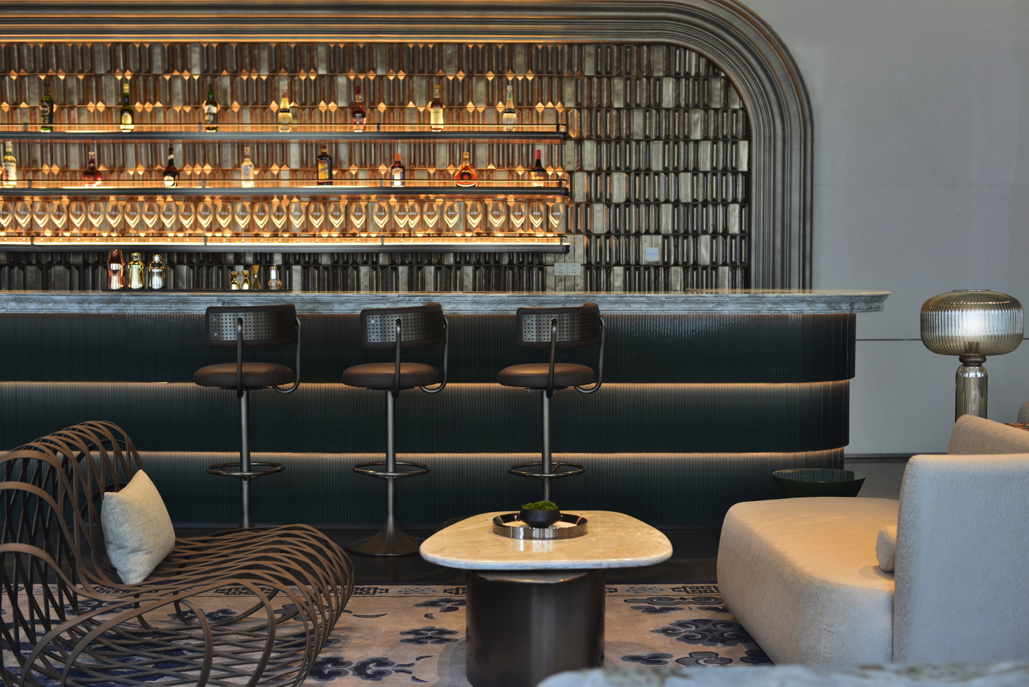 Luxurious hotel lounge with elegant furniture, soft lighting, and a marble bar. The modern design features curved architecture, plush seating, and warm tones.