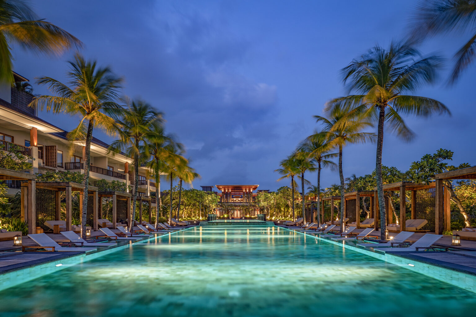Relax at a luxury beachfront resort in Bali, featuring a stunning infinity pool lined with palm trees, elegant cabanas, and breathtaking evening views.