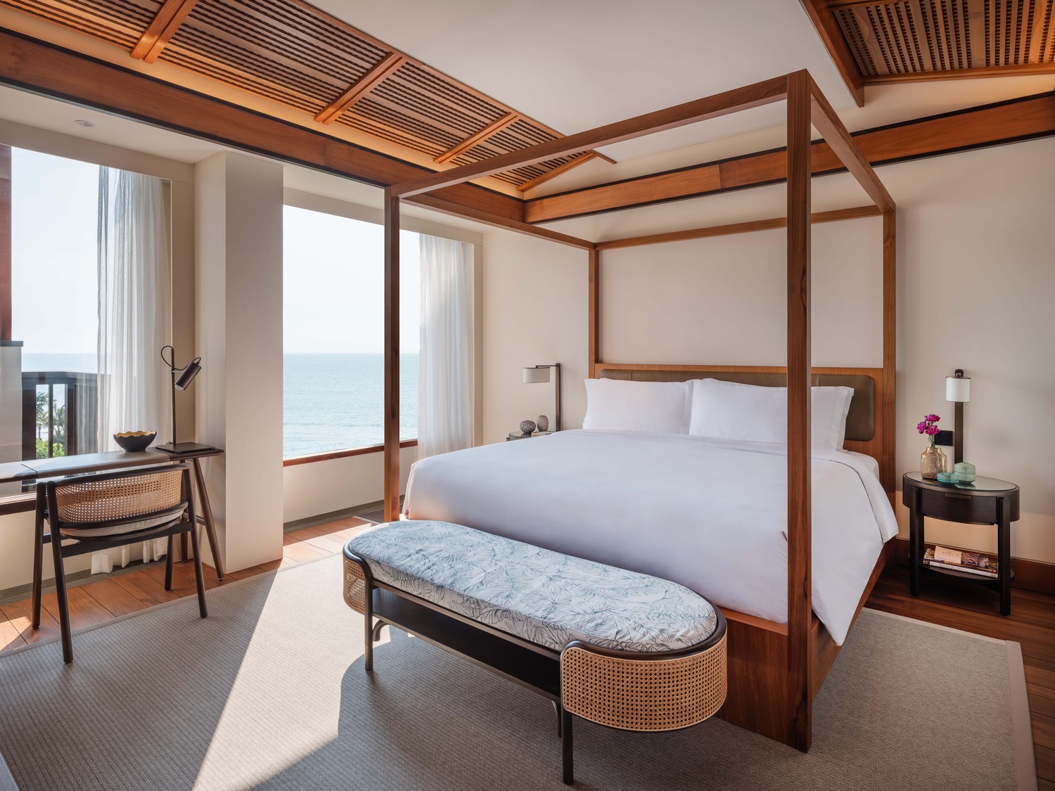 Luxurious hotel suite with a large bed, modern furnishings, and glass doors leading to a lush garden. Natural light and warm tones create a serene atmosphere.