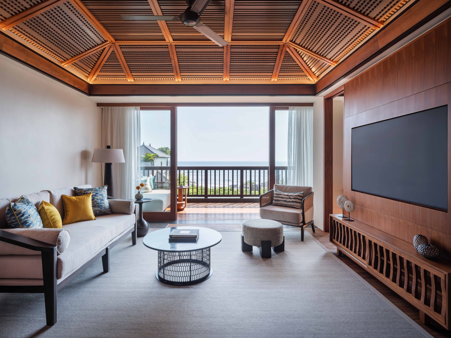 Luxurious hotel suite with a large bed, modern furnishings, and glass doors leading to a lush garden. Natural light and warm tones create a serene atmosphere.