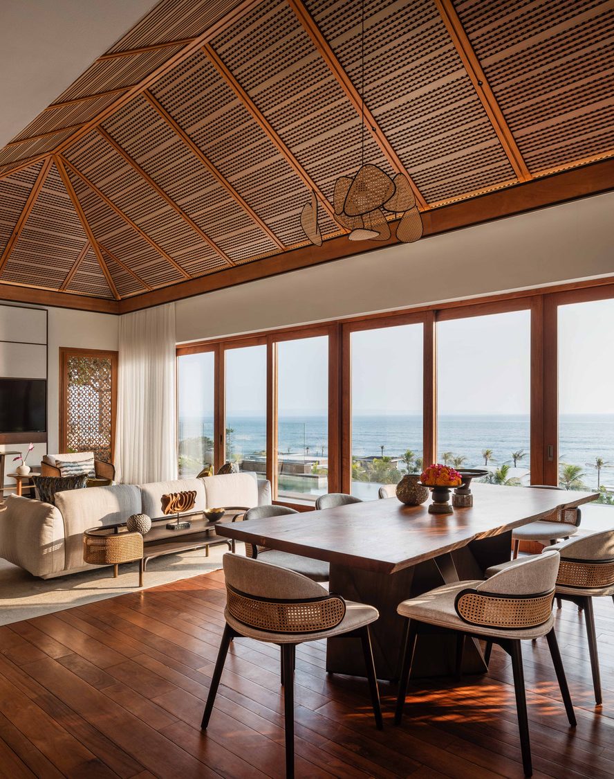Luxurious hotel suite with a large bed, modern furnishings, and glass doors leading to a lush garden. Natural light and warm tones create a serene atmosphere.