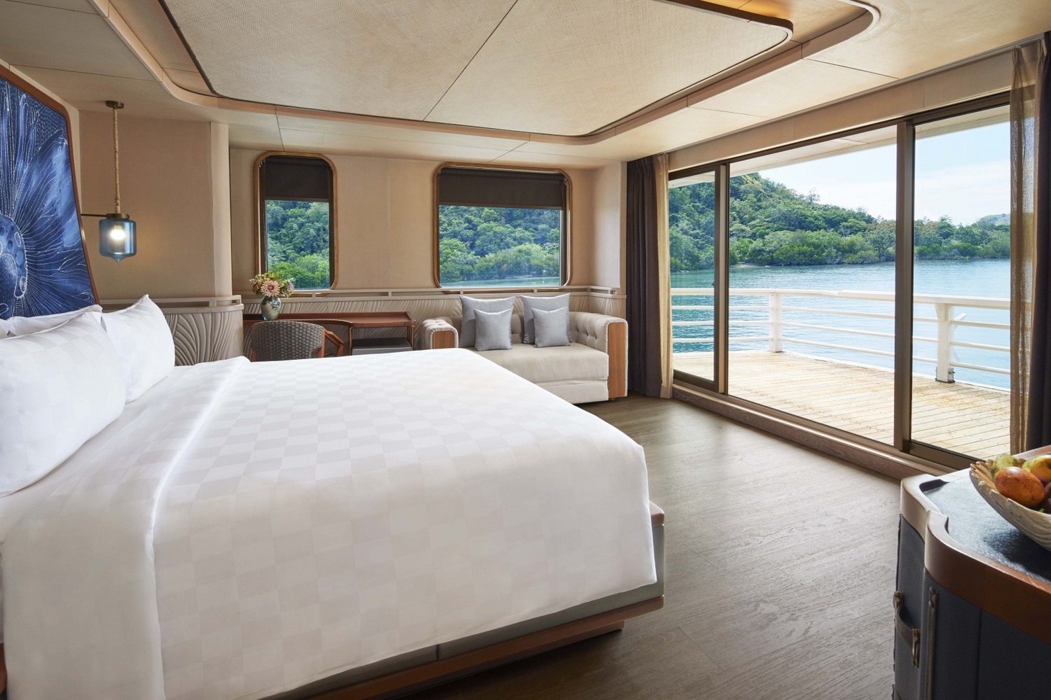 Luxurious yacht cabin with a king-sized bed, white linens, and a vibrant blue abstract headboard. Soft lighting and modern decor create a serene atmosphere.