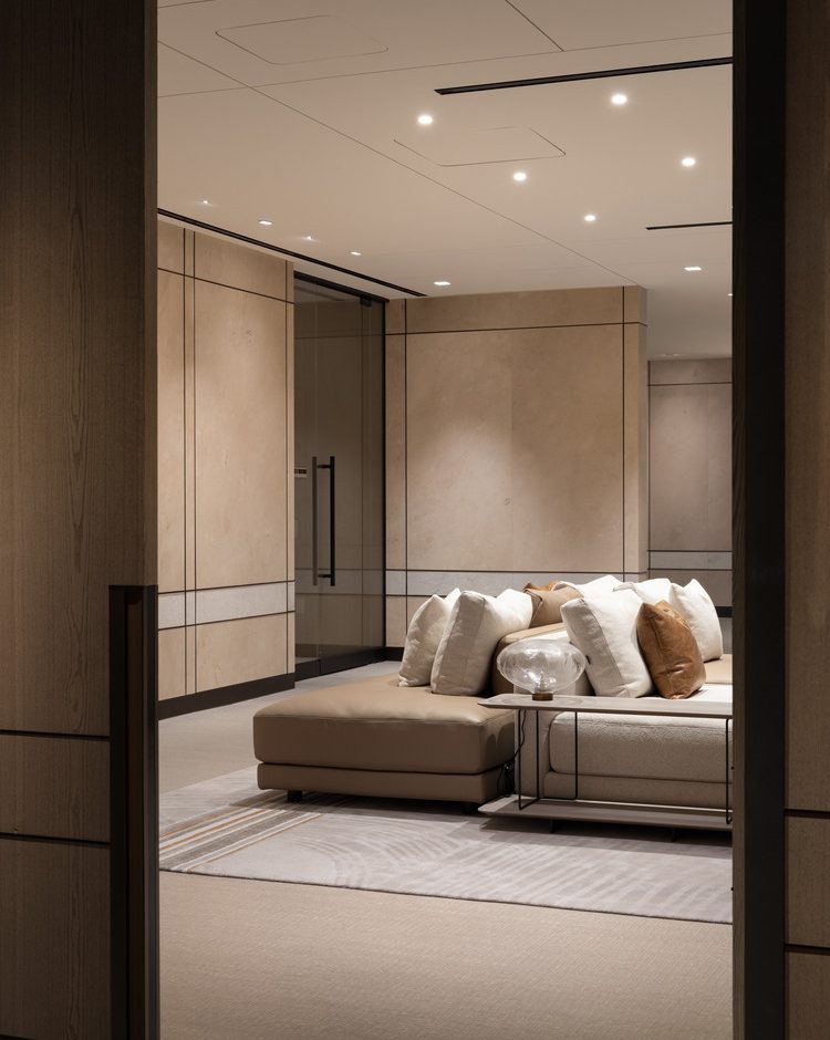 Sophisticated modern office lounge with beige decor, plush seating, and a sleek glass fireplace. Floor-to-ceiling windows and greenery create an airy, relaxing atmosphere.