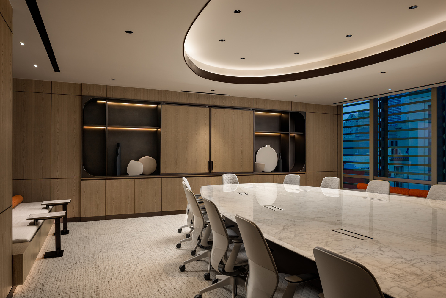 Sophisticated modern office lounge with beige decor, plush seating, and a sleek glass fireplace. Floor-to-ceiling windows and greenery create an airy, relaxing atmosphere.