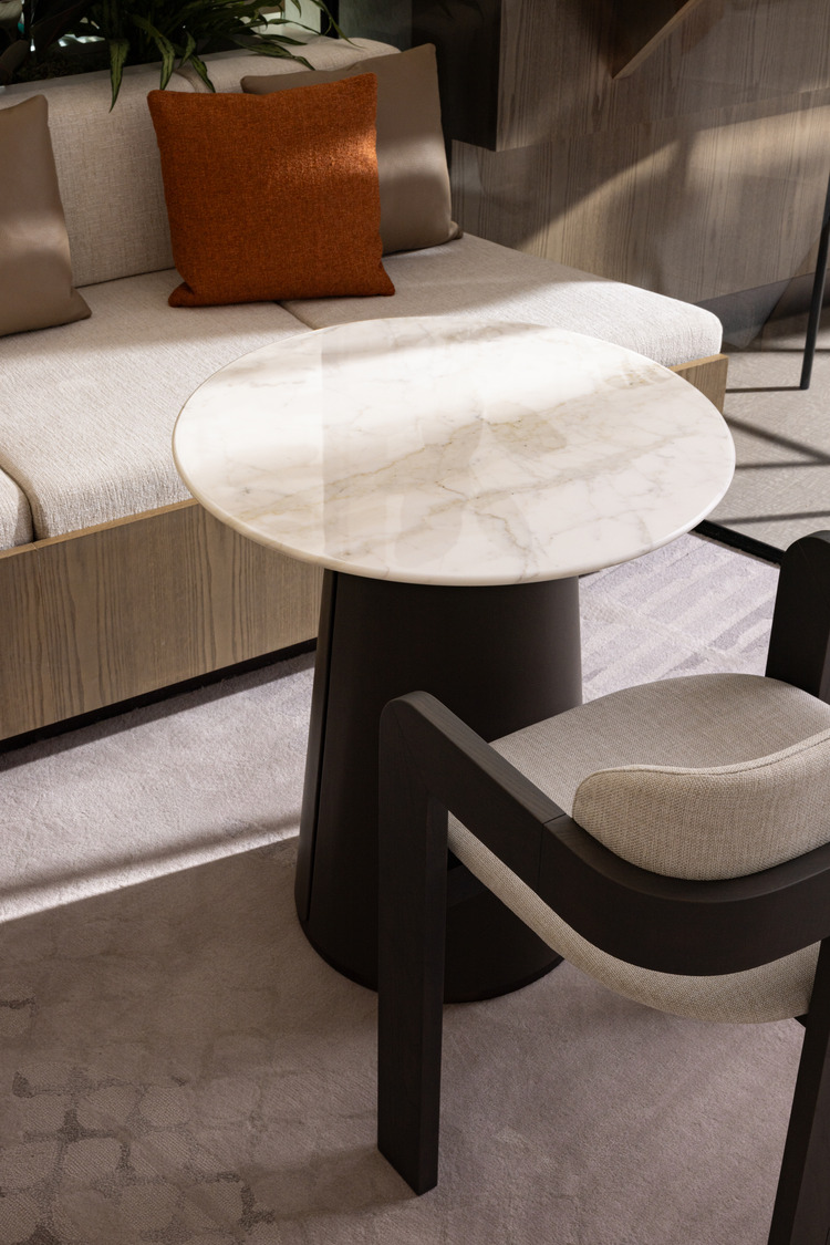 Sophisticated modern office lounge with beige decor, plush seating, and a sleek glass fireplace. Floor-to-ceiling windows and greenery create an airy, relaxing atmosphere.