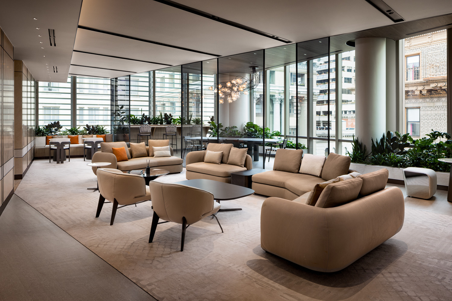 Sophisticated modern office lounge with beige decor, plush seating, and a sleek glass fireplace. Floor-to-ceiling windows and greenery create an airy, relaxing atmosphere.