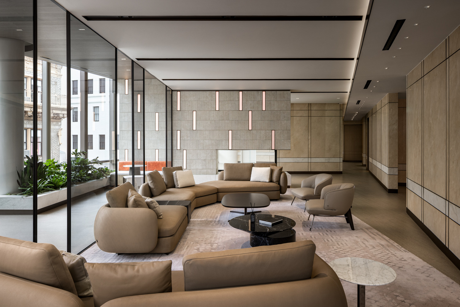 Sophisticated modern office lounge with beige decor, plush seating, and a sleek glass fireplace. Floor-to-ceiling windows and greenery create an airy, relaxing atmosphere.