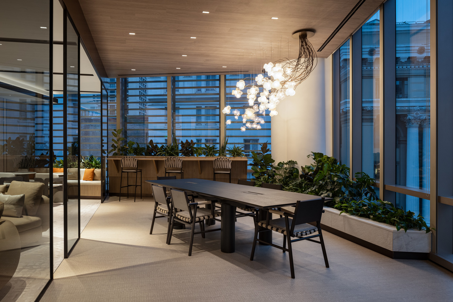Sophisticated modern office lounge with beige decor, plush seating, and a sleek glass fireplace. Floor-to-ceiling windows and greenery create an airy, relaxing atmosphere.