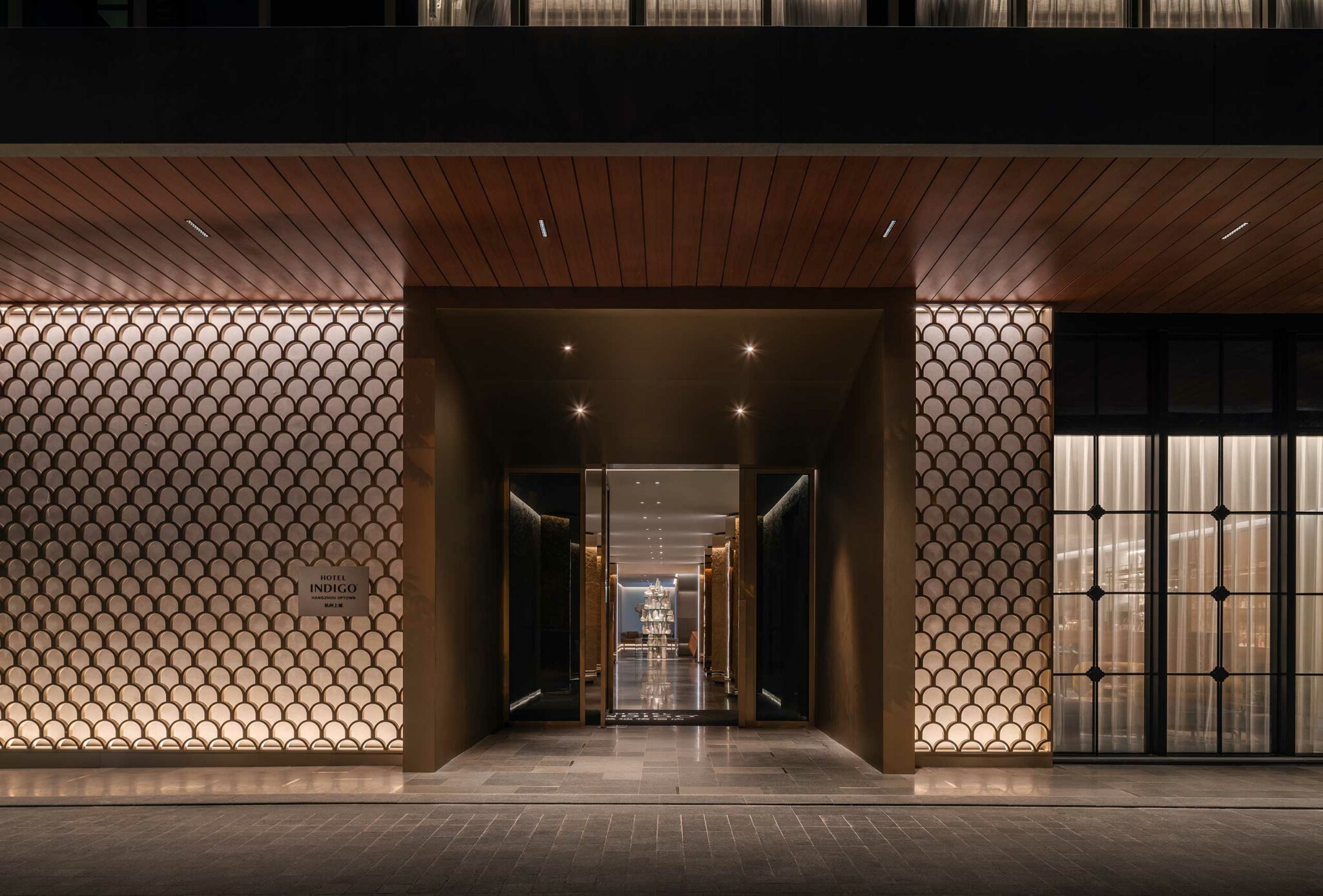 Luxurious hotel entrance at night with warm lighting. Features geometric wall patterns and a long hallway, creating an inviting and elegant atmosphere.