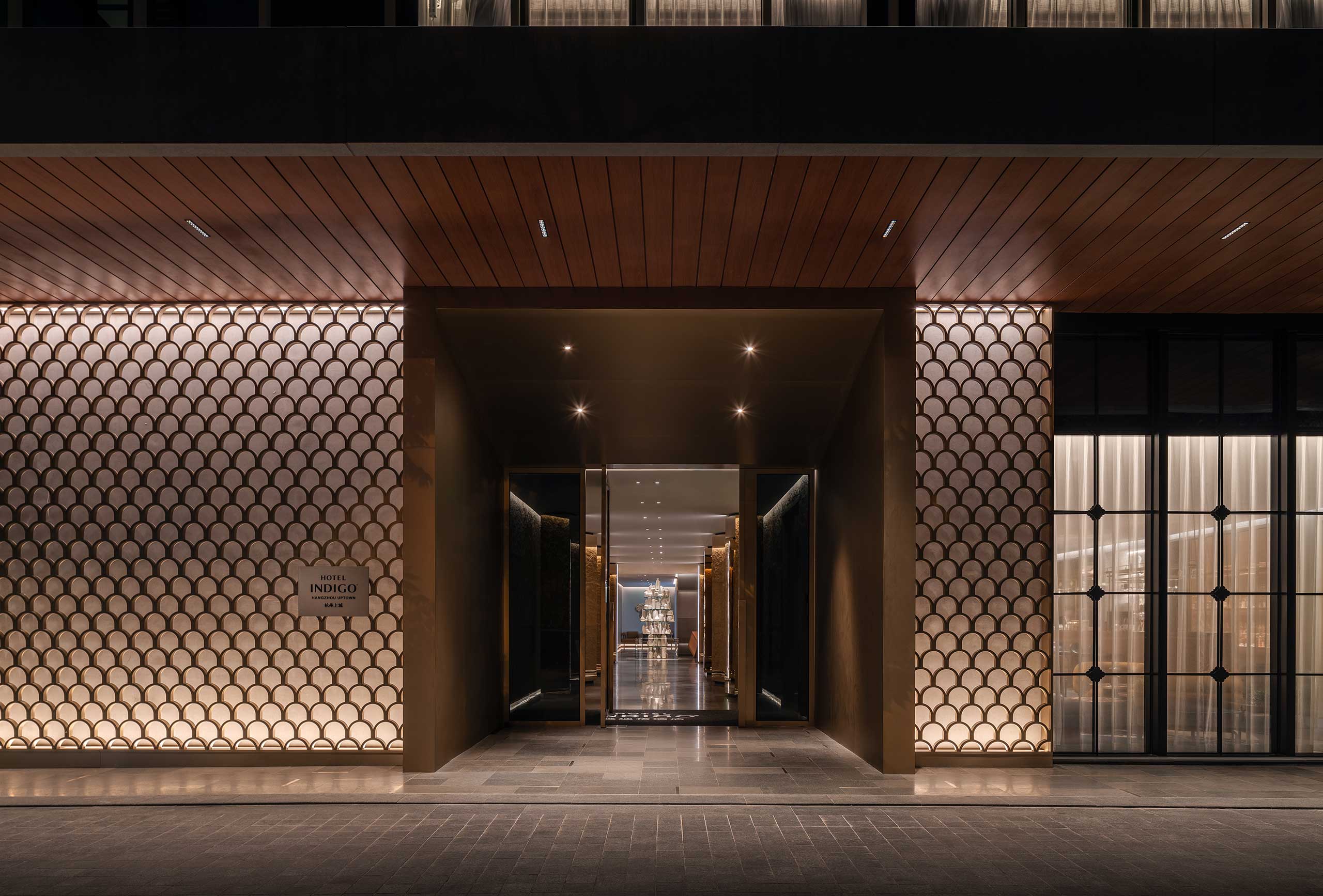 Luxurious hotel entrance at night with warm lighting. Features geometric wall patterns and a long hallway, creating an inviting and elegant atmosphere.