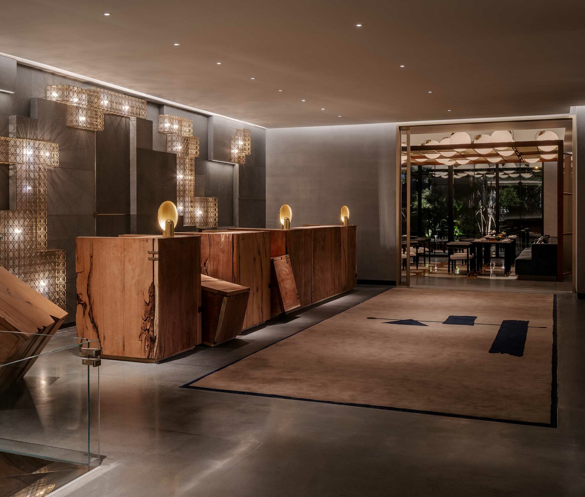 Elegant hotel lobby with modern design. Features a wooden reception desk, artistic wall lights, and a glass shelf displaying white vases. Warm, inviting ambiance.
