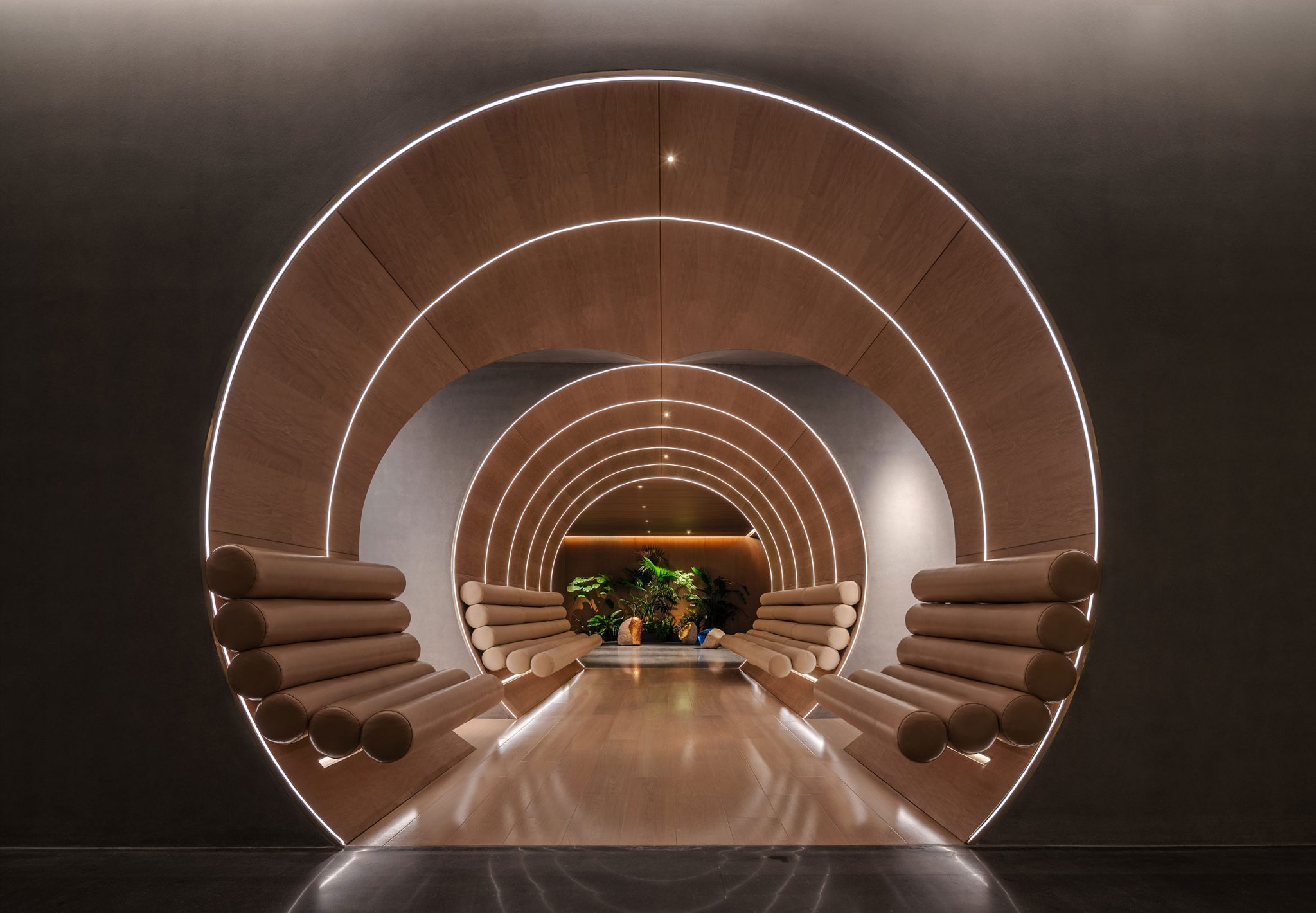 Futuristic hotel hallway with concentric wooden arches and cushioned seats, softly lit with white LED strips. Green plants at the end create a serene ambiance.