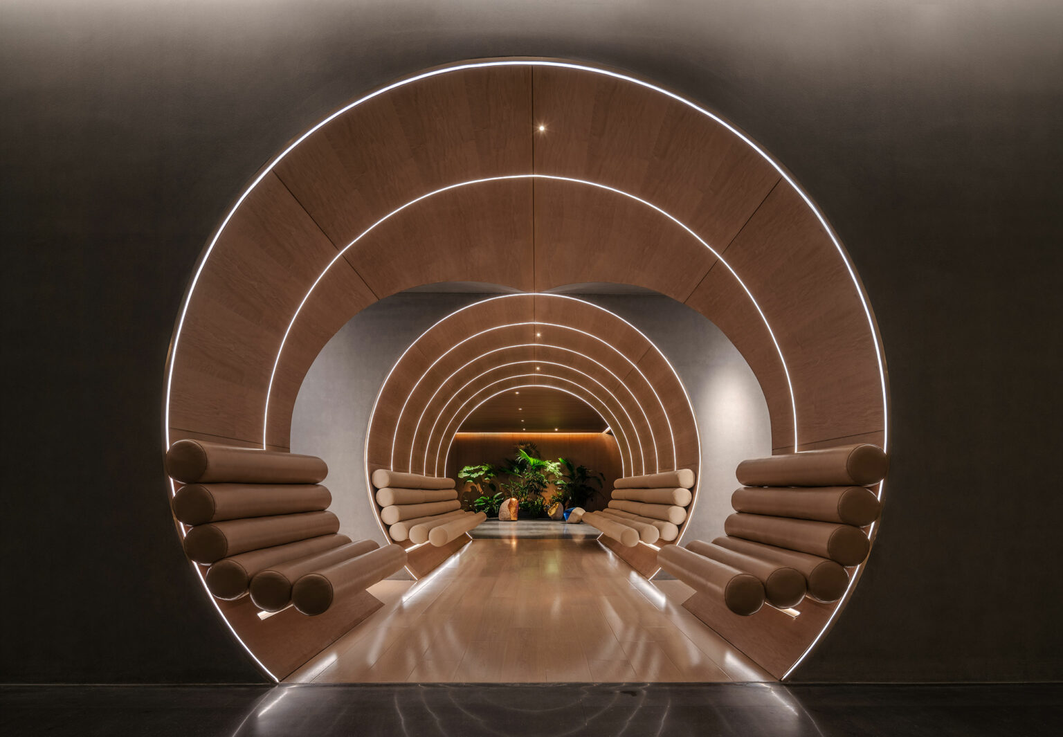 Futuristic hotel hallway with concentric wooden arches and cushioned seats, softly lit with white LED strips. Green plants at the end create a serene ambiance.