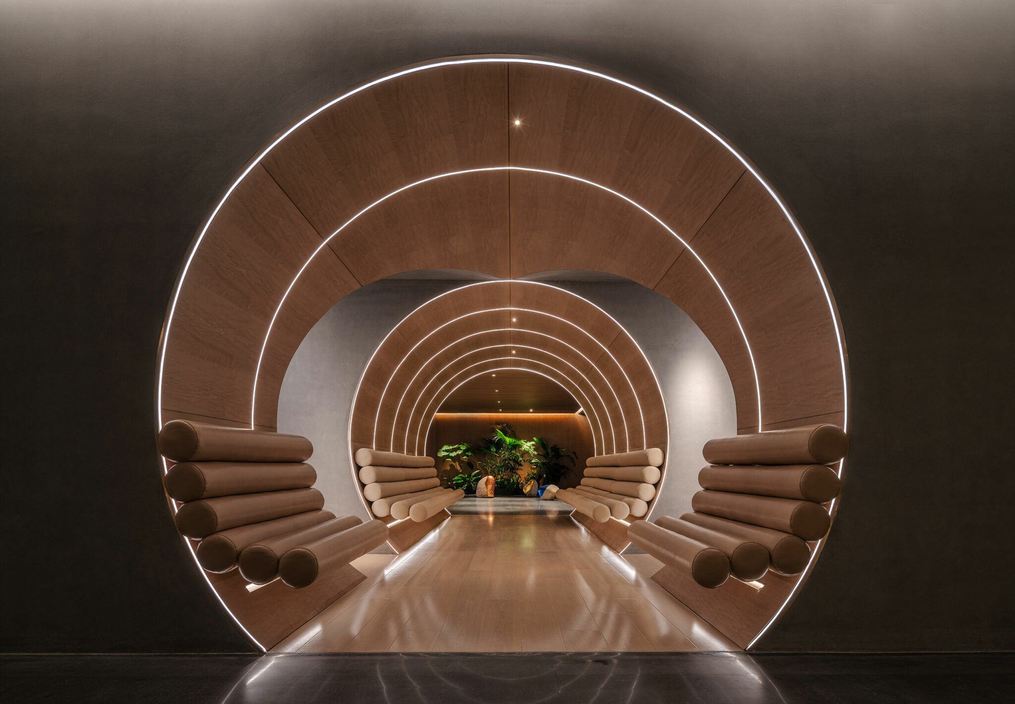 Futuristic hotel hallway with concentric wooden arches and cushioned seats, softly lit with white LED strips. Green plants at the end create a serene ambiance.