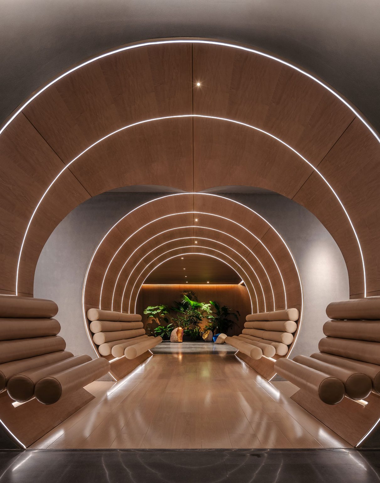 Futuristic hotel hallway with concentric wooden arches and cushioned seats, softly lit with white LED strips. Green plants at the end create a serene ambiance.