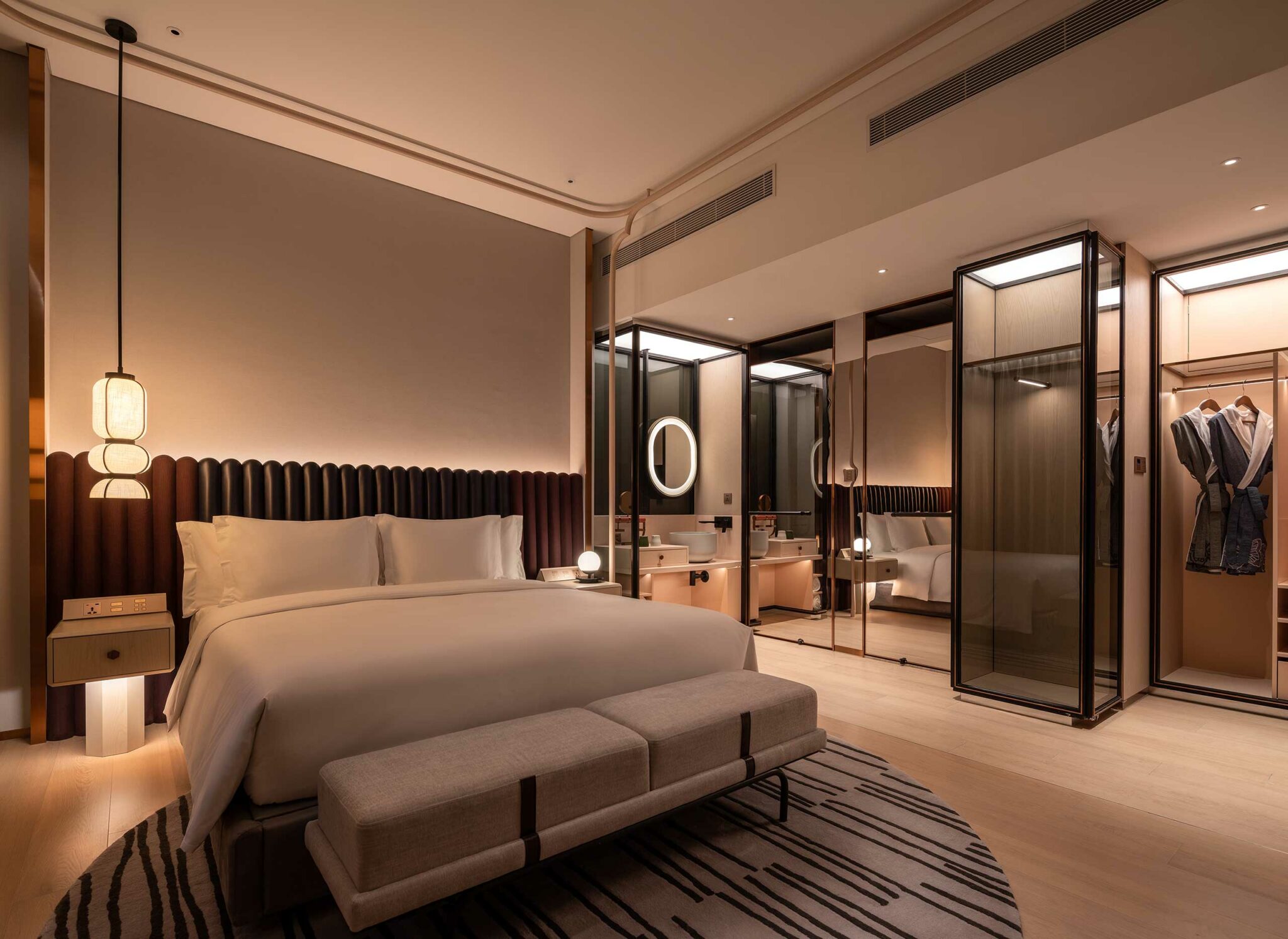Elegant hotel room with a plush king-size bed, modern pendant lighting, and a sleek en-suite bathroom. Neutral tones create a calm, luxurious ambiance.