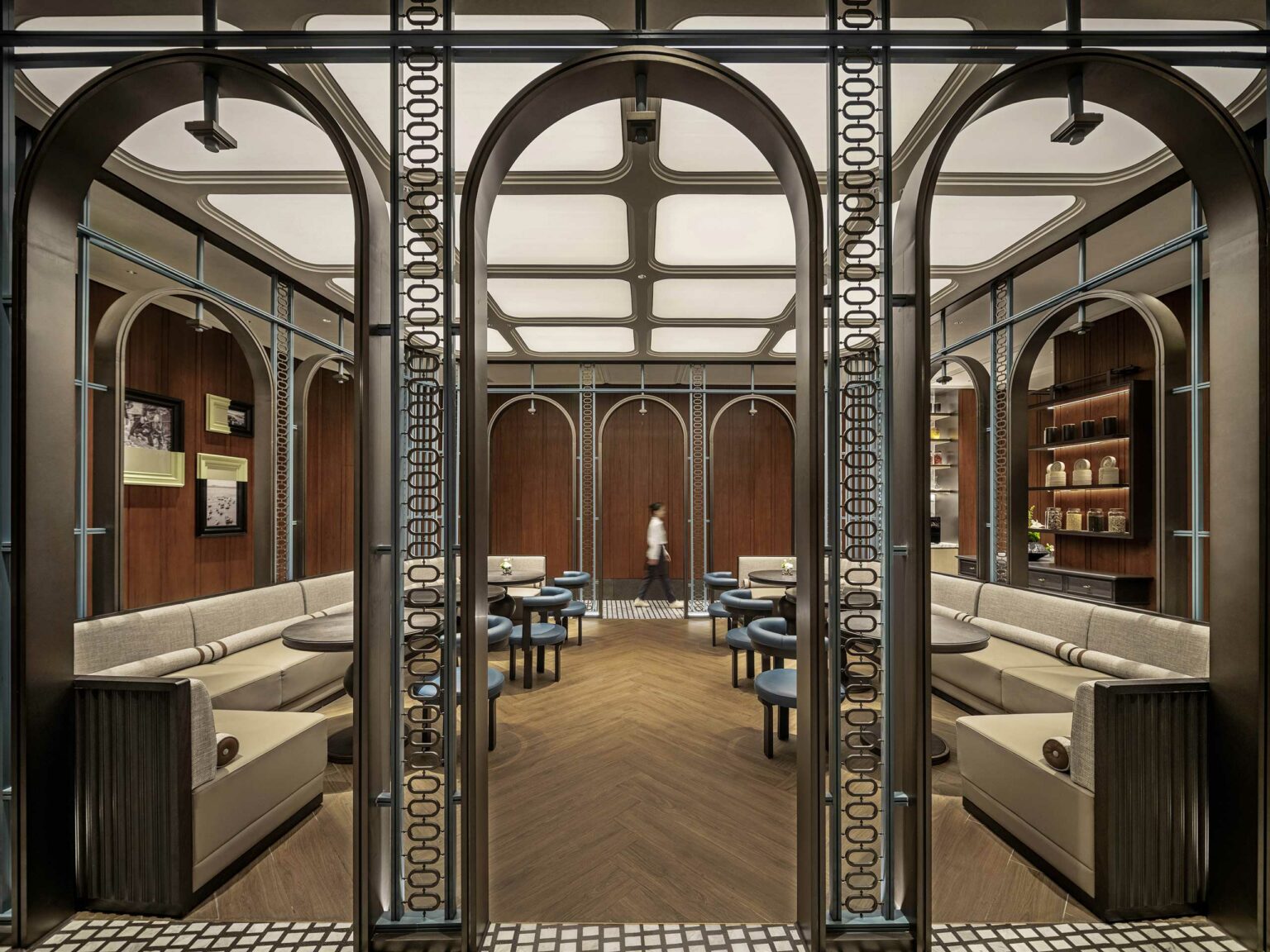 Modern hotel restaurant interior with elegant arches and symmetry. Cozy beige seating and wooden tables on a geometric-patterned floor; soft ambient lighting enhances warmth.