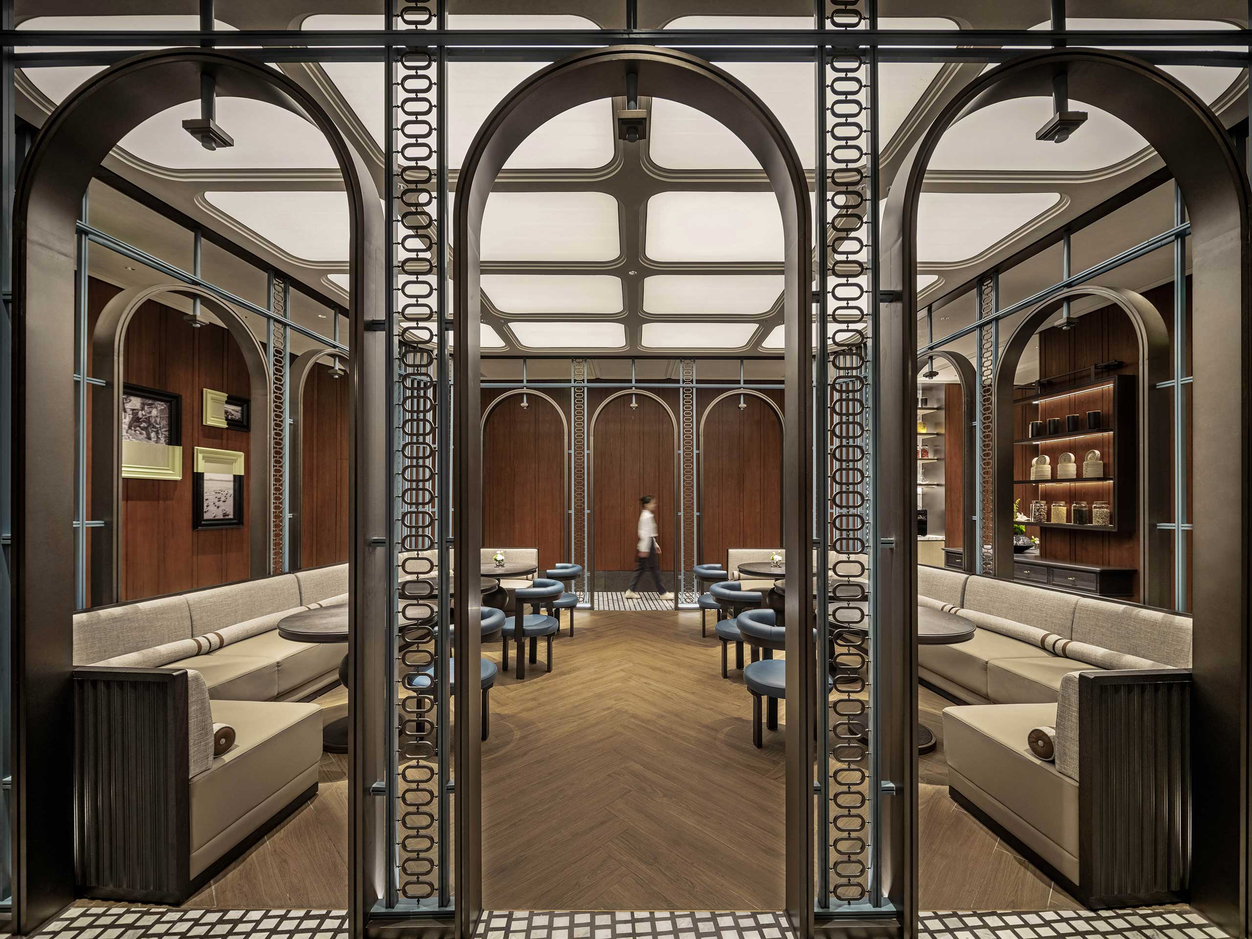 Modern hotel restaurant interior with elegant arches and symmetry. Cozy beige seating and wooden tables on a geometric-patterned floor; soft ambient lighting enhances warmth.