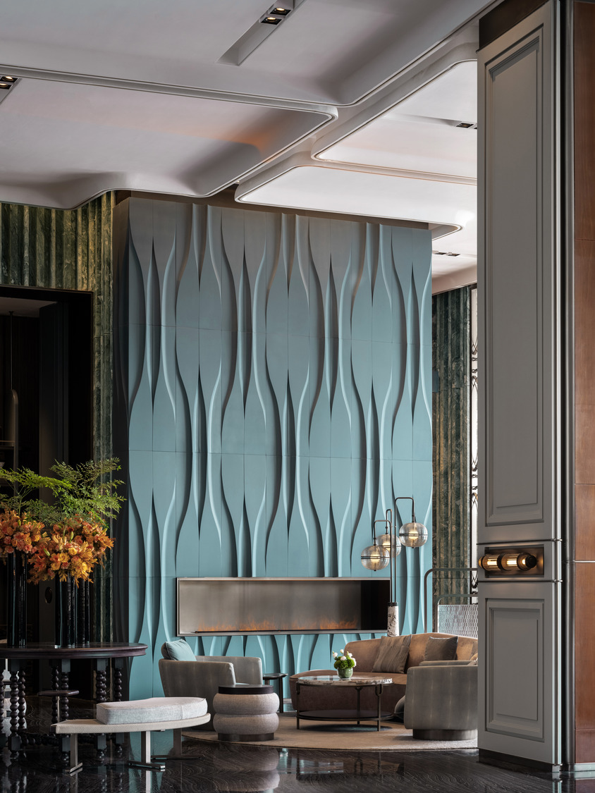 Luxurious hotel lounge with modern decor, featuring a wavy teal wall, linear fireplace, round seating, ambient lighting, and a leafy green plant.
