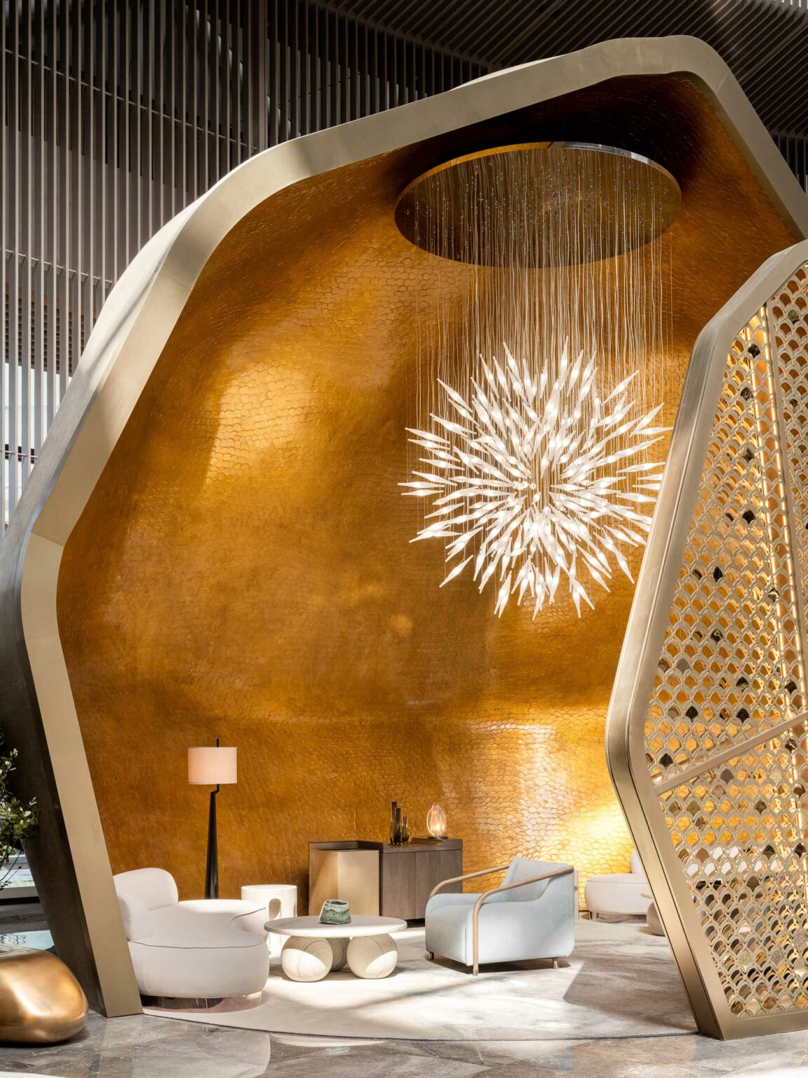 Luxurious hotel spa lounge with gold hexagonal walls and an abstract chandelier. Features modern white chairs, a lamp, and a stylish divider, conveying opulence.