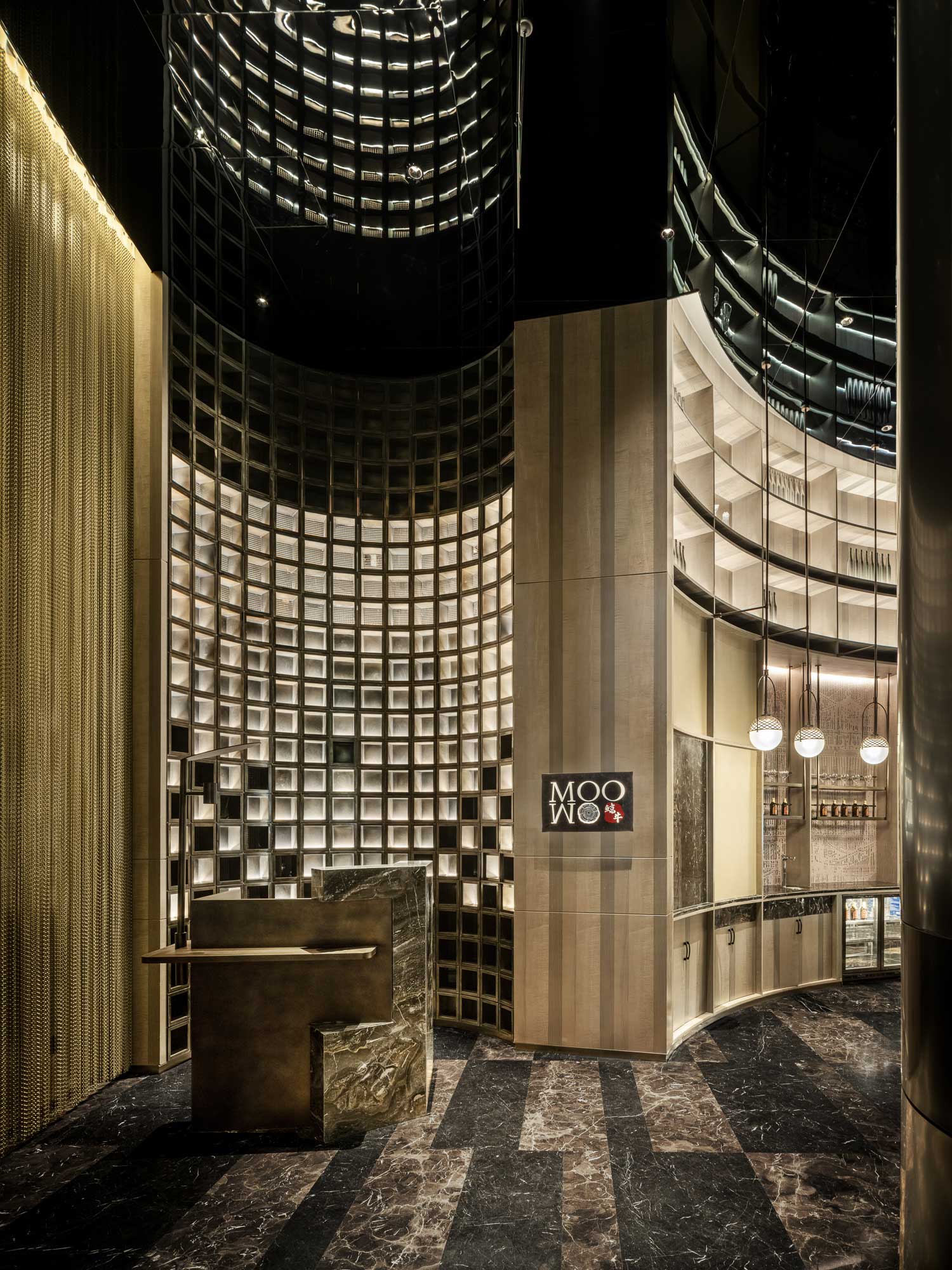 Stylish hotel restaurant interior with tall, curved wooden walls, intricate shelving, and lit orb chandeliers.