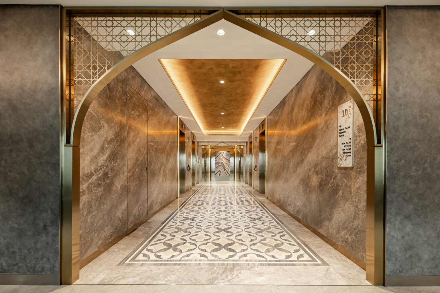 Elegant arched office lift lobby with gold accents, polished marble walls, ornate geometric ceiling, and patterned floor tiles.