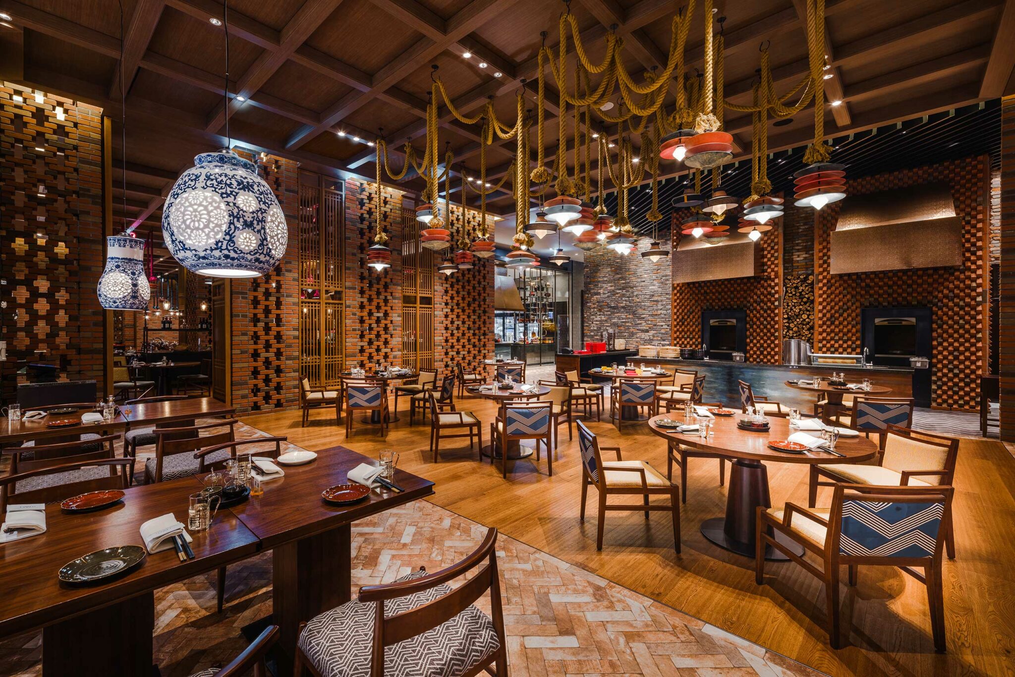 Elegant restaurant interior of a luxurious resort with warm lighting, intricate hanging lamps, wooden tables set for dining, and a cozy, inviting atmosphere.