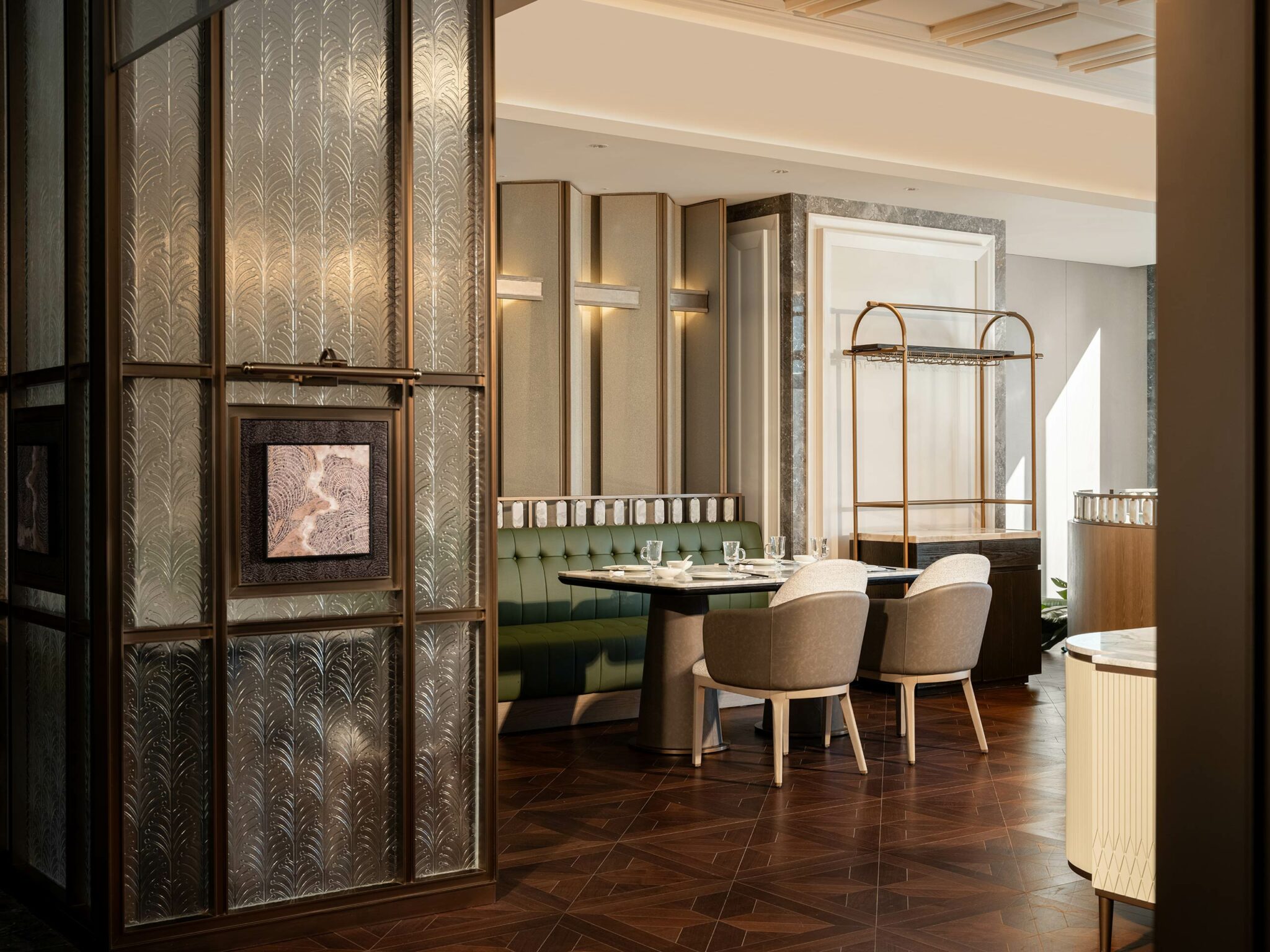 Luxurious hotel all day dining area with a green tufted bench, two beige chairs, and dark wood table. Art Deco wall panels and parquet flooring add elegance.