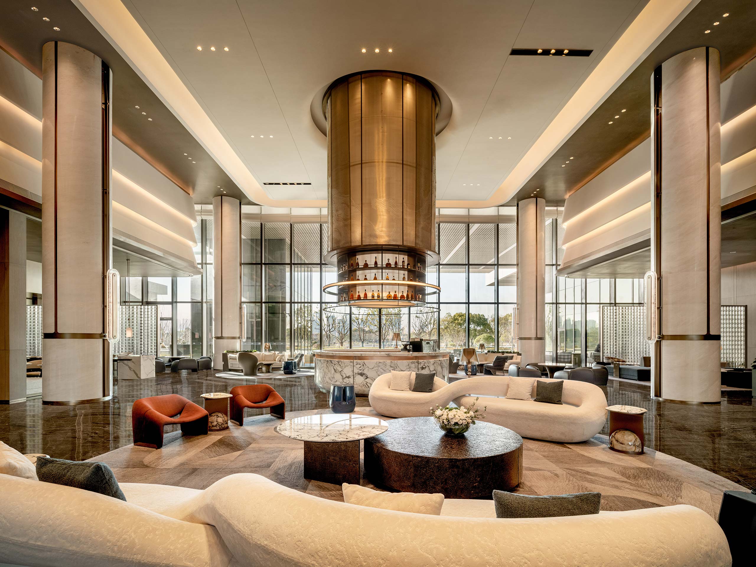 Luxurious hotel lobby with a central circular bar, modern sofas, and large windows. Warm lighting creates an elegant and inviting atmosphere.