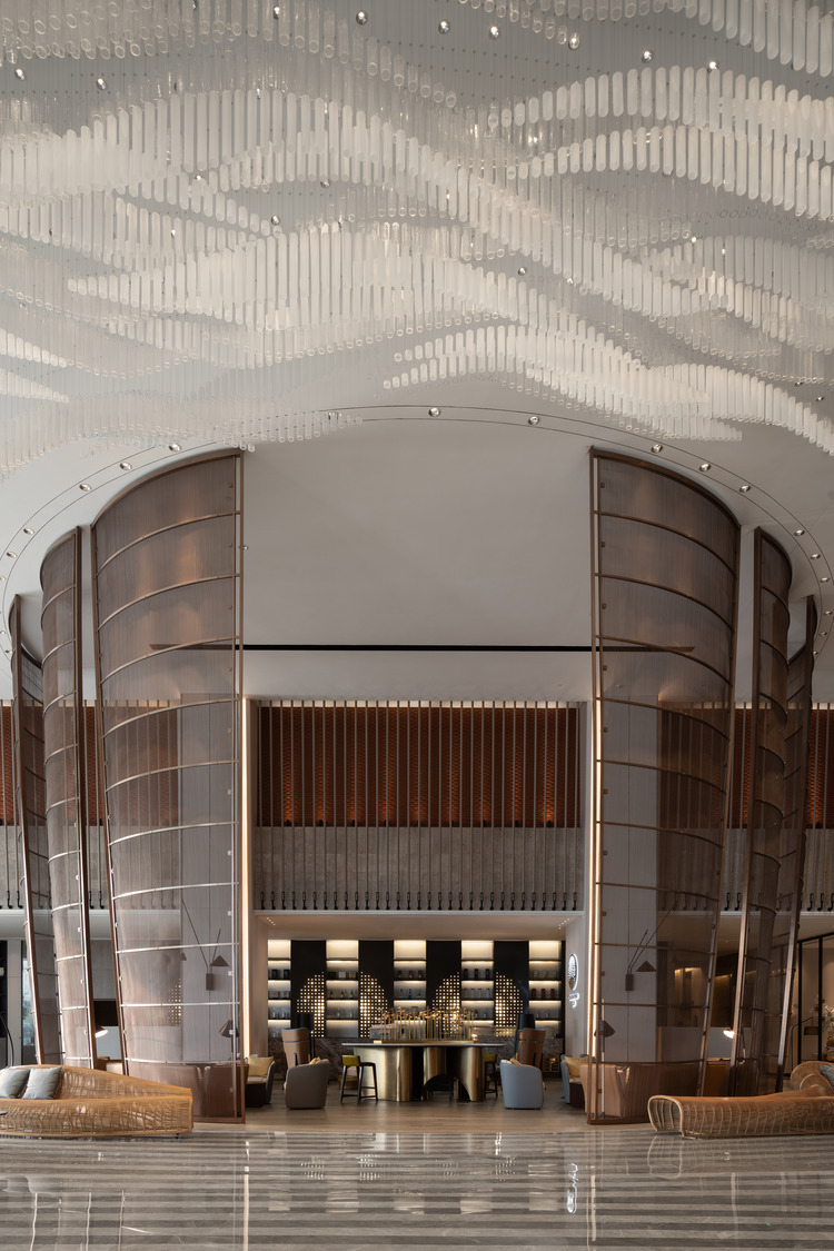 A contemporary restaurant entryway featuring textured wooden walls, a striking circular chandelier, and stylish accent tables, creating a welcoming and elegant atmosphere for guests in a luxury setting.