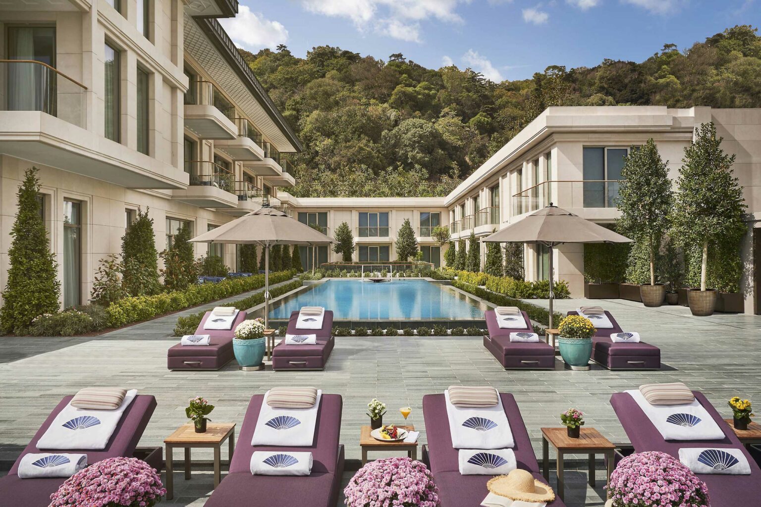 Elegant hotel courtyard with a serene pool, surrounded by luxurious loungers and umbrellas. The atmosphere is calm and inviting, embraced by lush greenery.