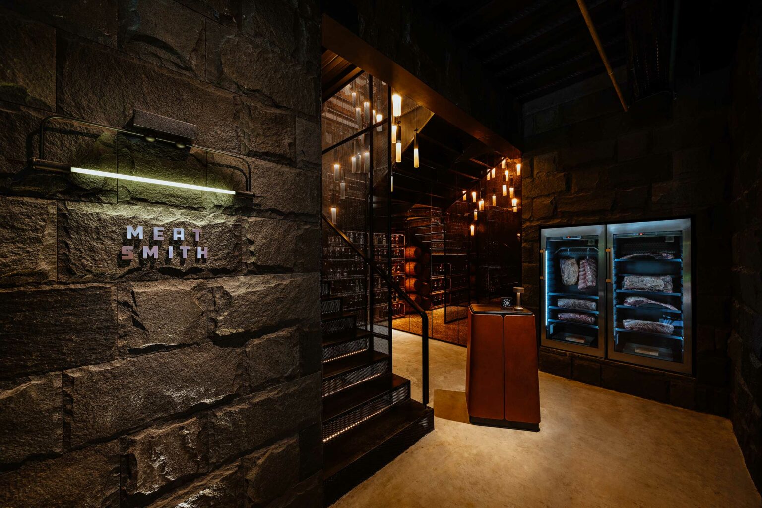 Dimly lit charcuterie area of a restaurant with stone walls, a sign reading