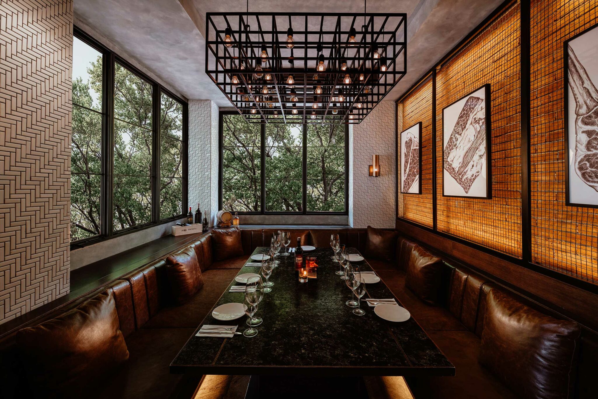 Cozy restaurant private dining room with a large, black marble table surrounded by brown leather seating. Warm lighting, wall art, and large windows overlook greenery.