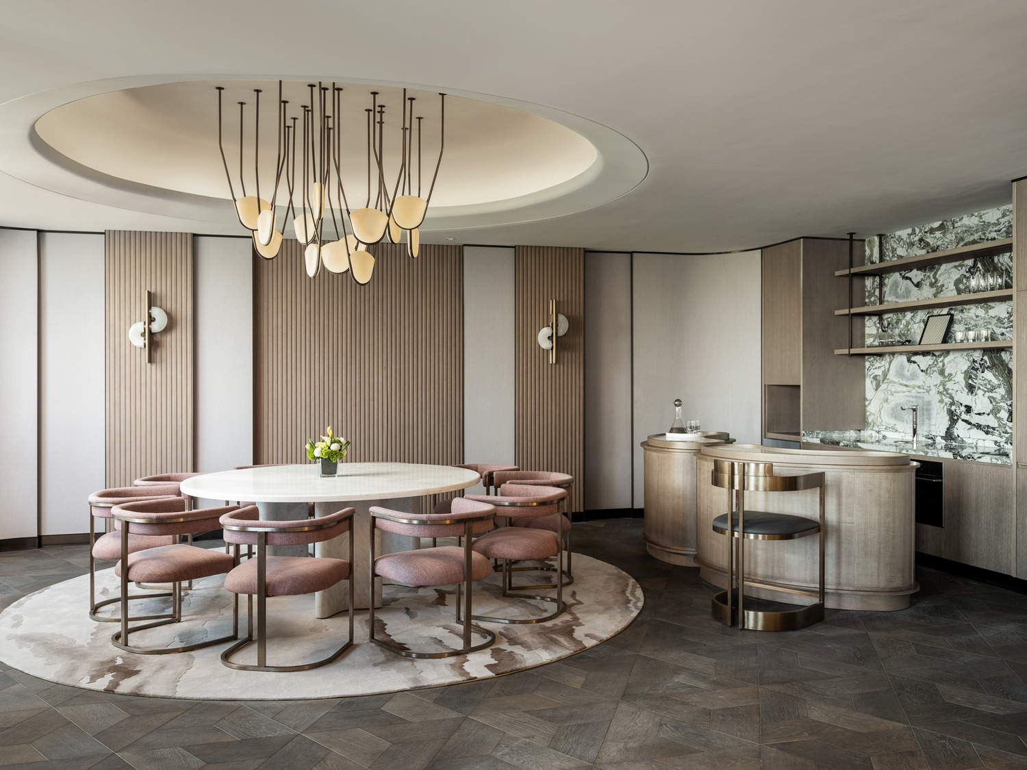 Modern suite room with elegant decor: round bed under soft lighting, marble TV wall divider, plush seating, and a small vase of flowers on a table.