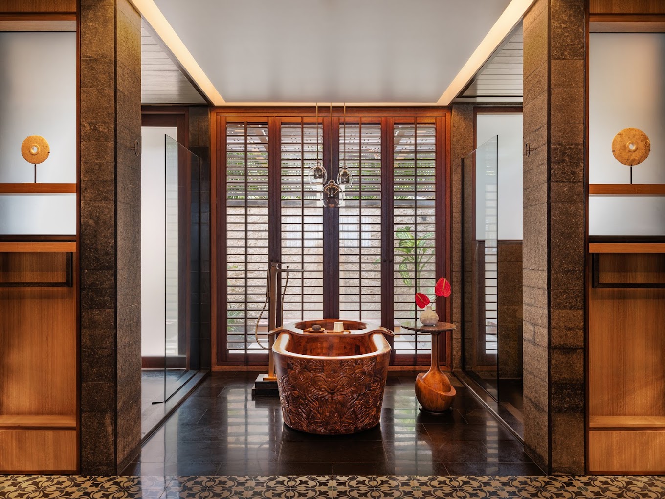 Luxurious suite bathroom with a carved wooden bathtub, large vertical windows with wooden shutters, hanging lights, and modern decor, creating an elegant ambiance.