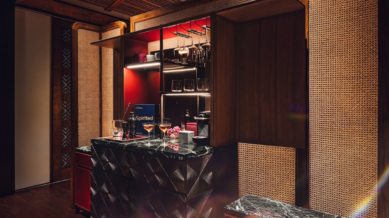 Stylish suite bar corner with marble counter, cocktail glasses, and bottles. Warm lighting, wooden accents, and textured panels create an inviting ambiance.