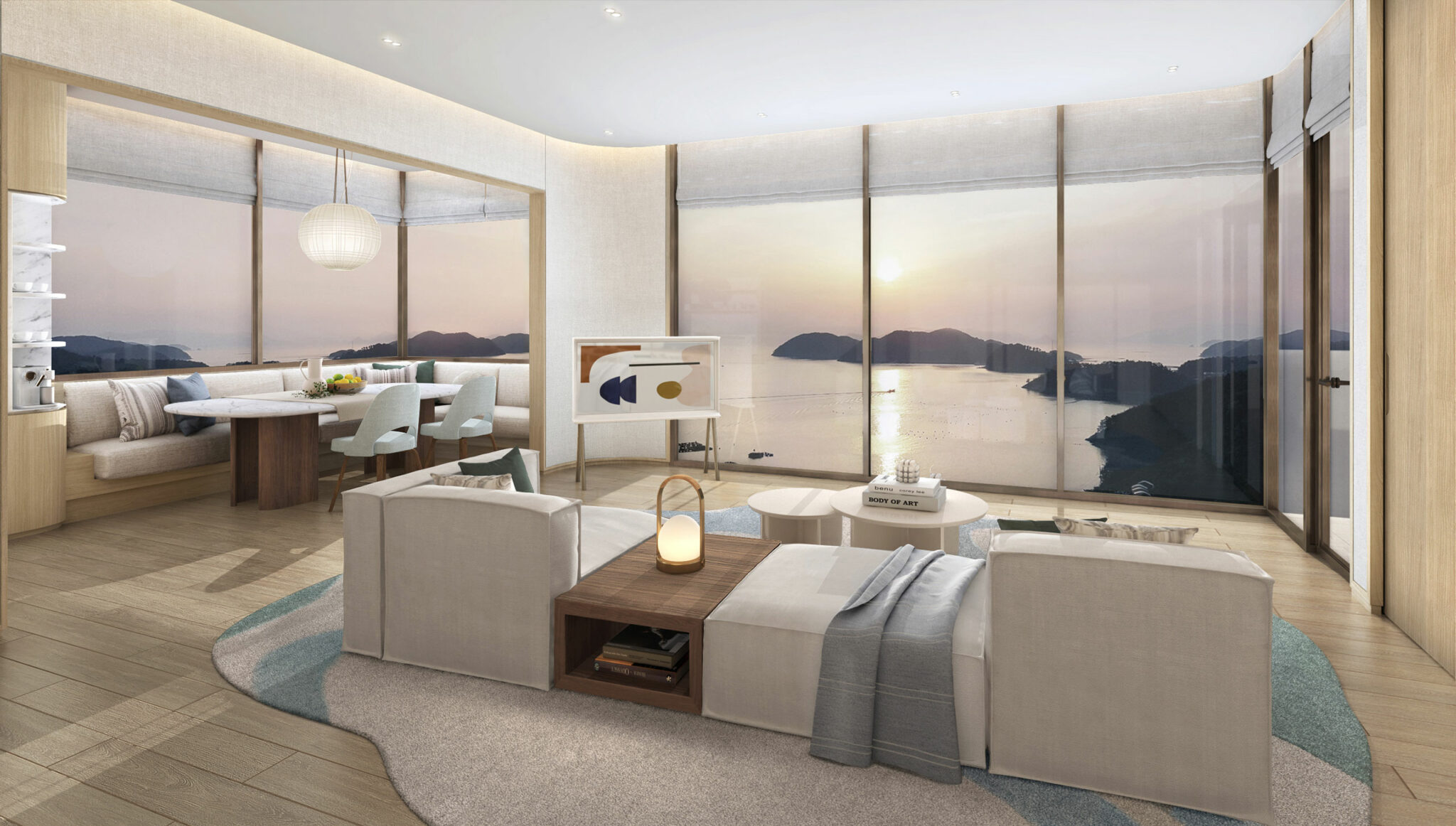 Modern resort suite living room with large windows showcasing a serene sunset over the ocean. Features plush white seating, a wooden dining table, and a soft ambiance.
