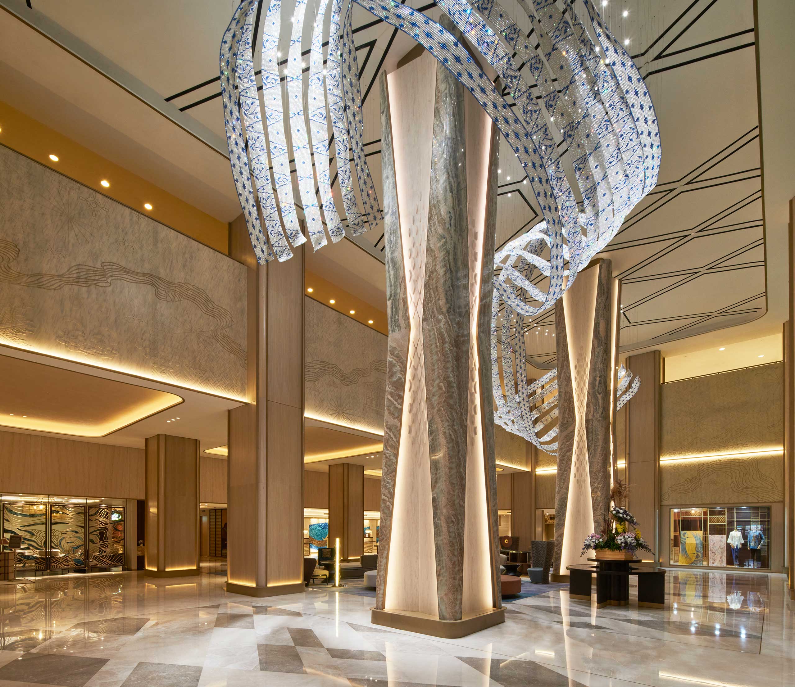 Spacious hotel lobby with tall, illuminated columns, sculptural ceiling art, warm lighting, and marble floors, conveying elegance and luxury.