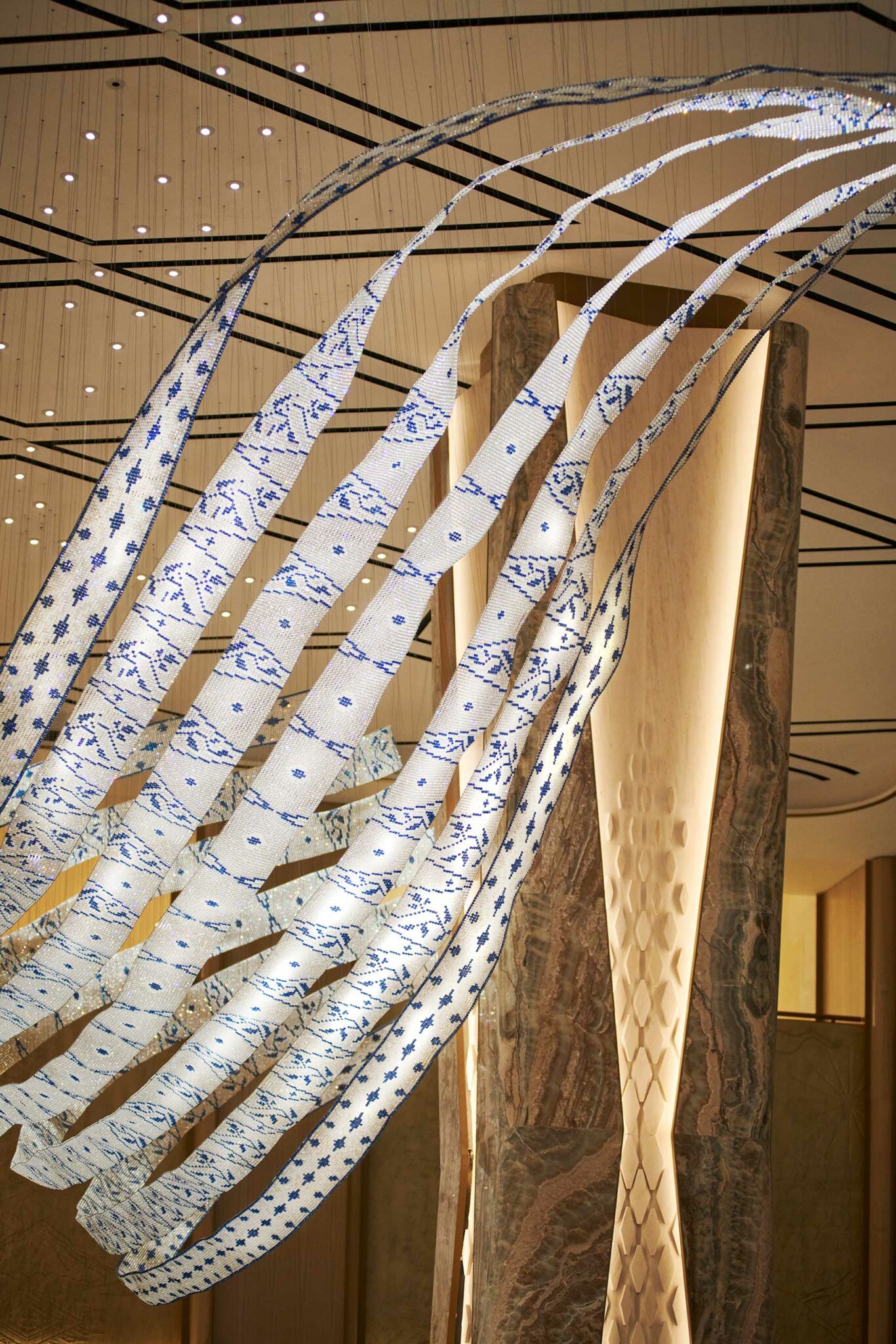 Elegant white and blue patterned ribbons curve gracefully in an art installation, set against a modern interior with warm lighting and marble textures.