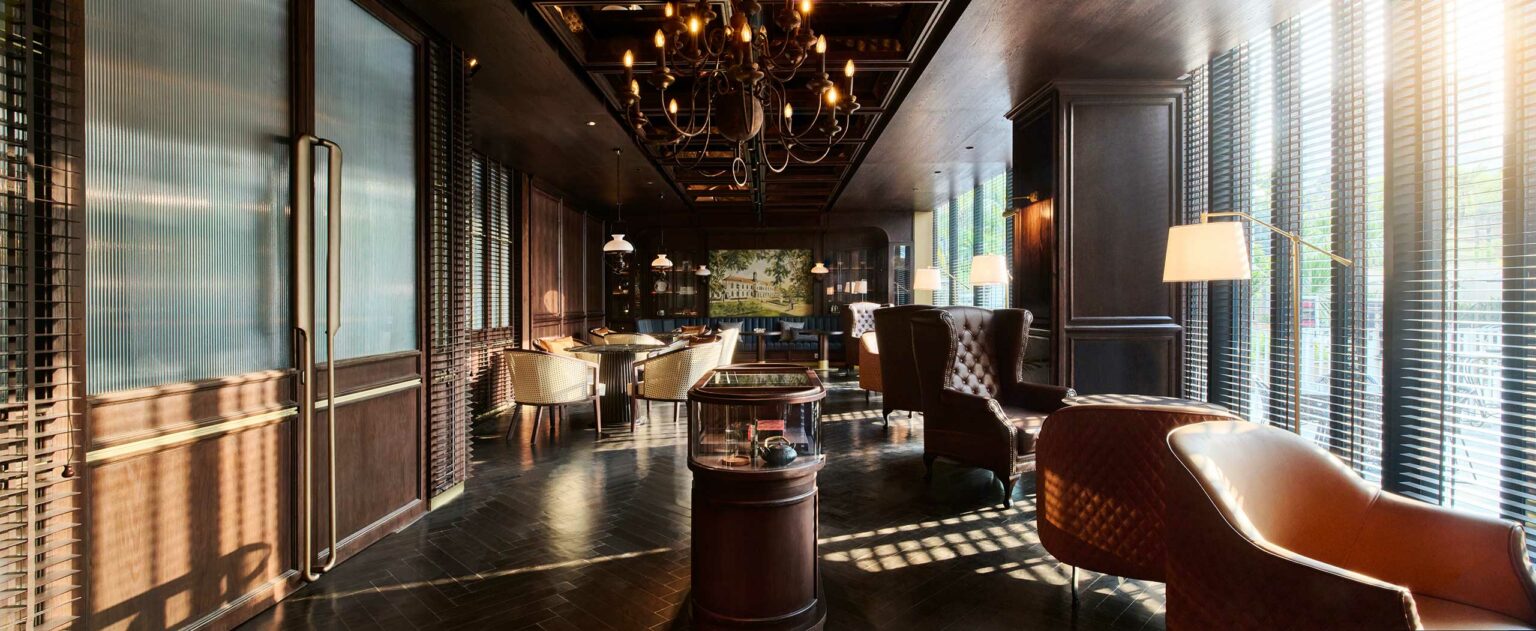 Spacious hotel lobby with a large, curved metal sculpture hanging from the ceiling. The room features warm lighting and contemporary wooden decor.