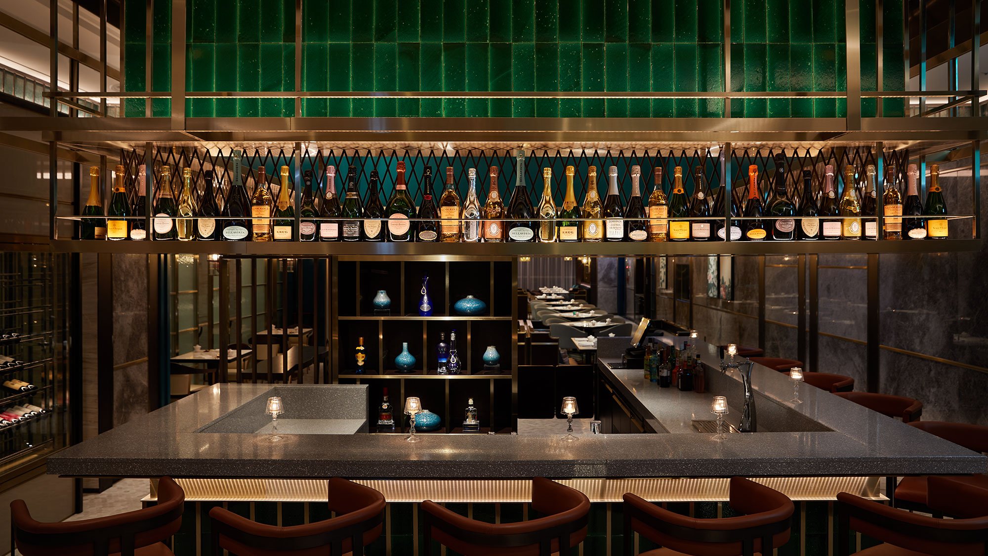 Elegant bar interior with row of champagne bottles on a shelf above a sleek countertop. Dim lighting creates a warm, sophisticated ambiance.
