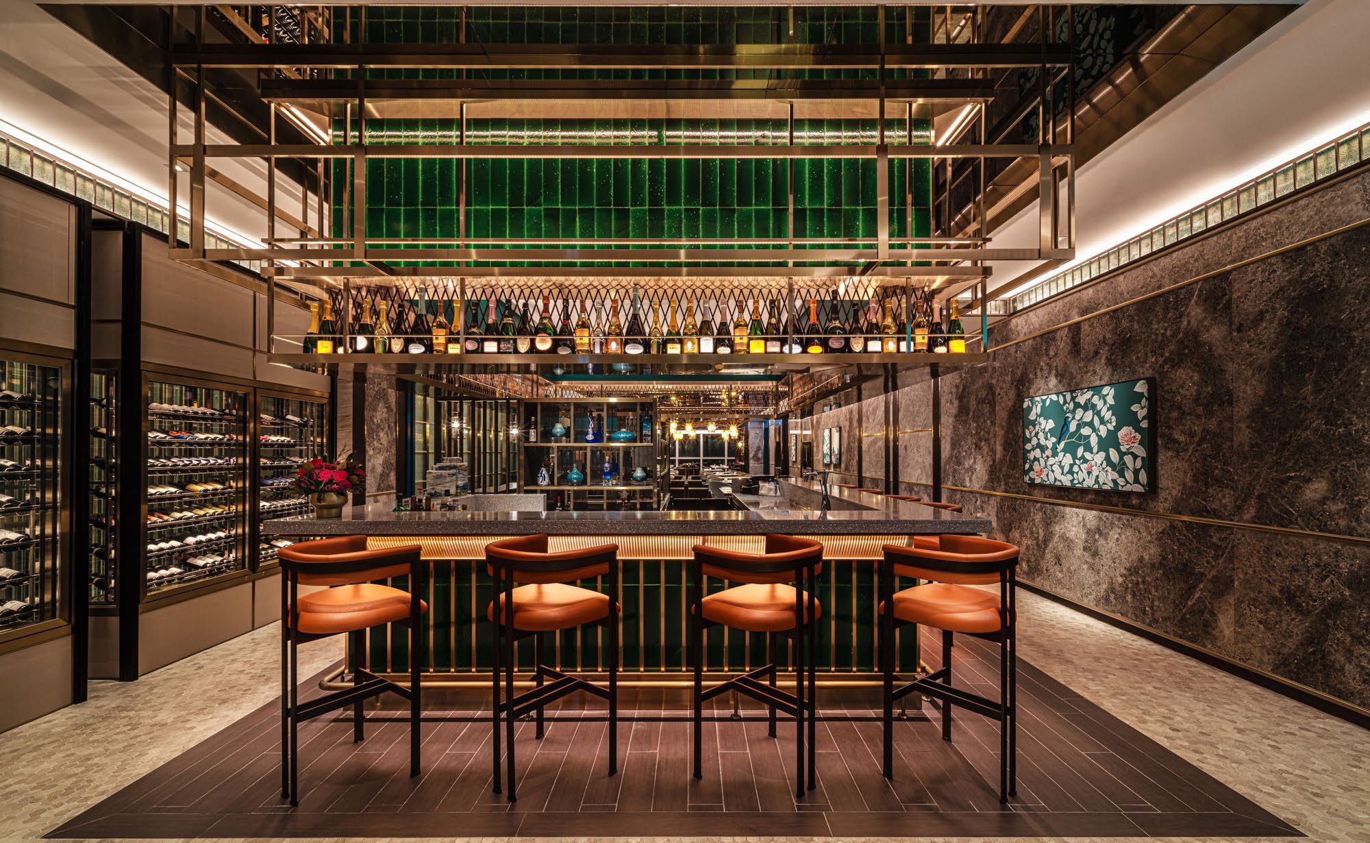 Luxurious restaurant bar counter featuring elegant lighting, a mirror backdrop, leather chairs, and art on dark walls. A sophisticated and inviting ambiance.