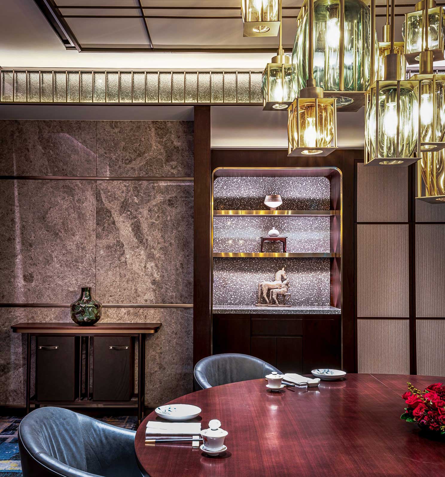 Luxurious hotel dining room with marble walls and elegant lighting. A round wooden table is set with dishes, and an art piece is displayed in a lit shelf.