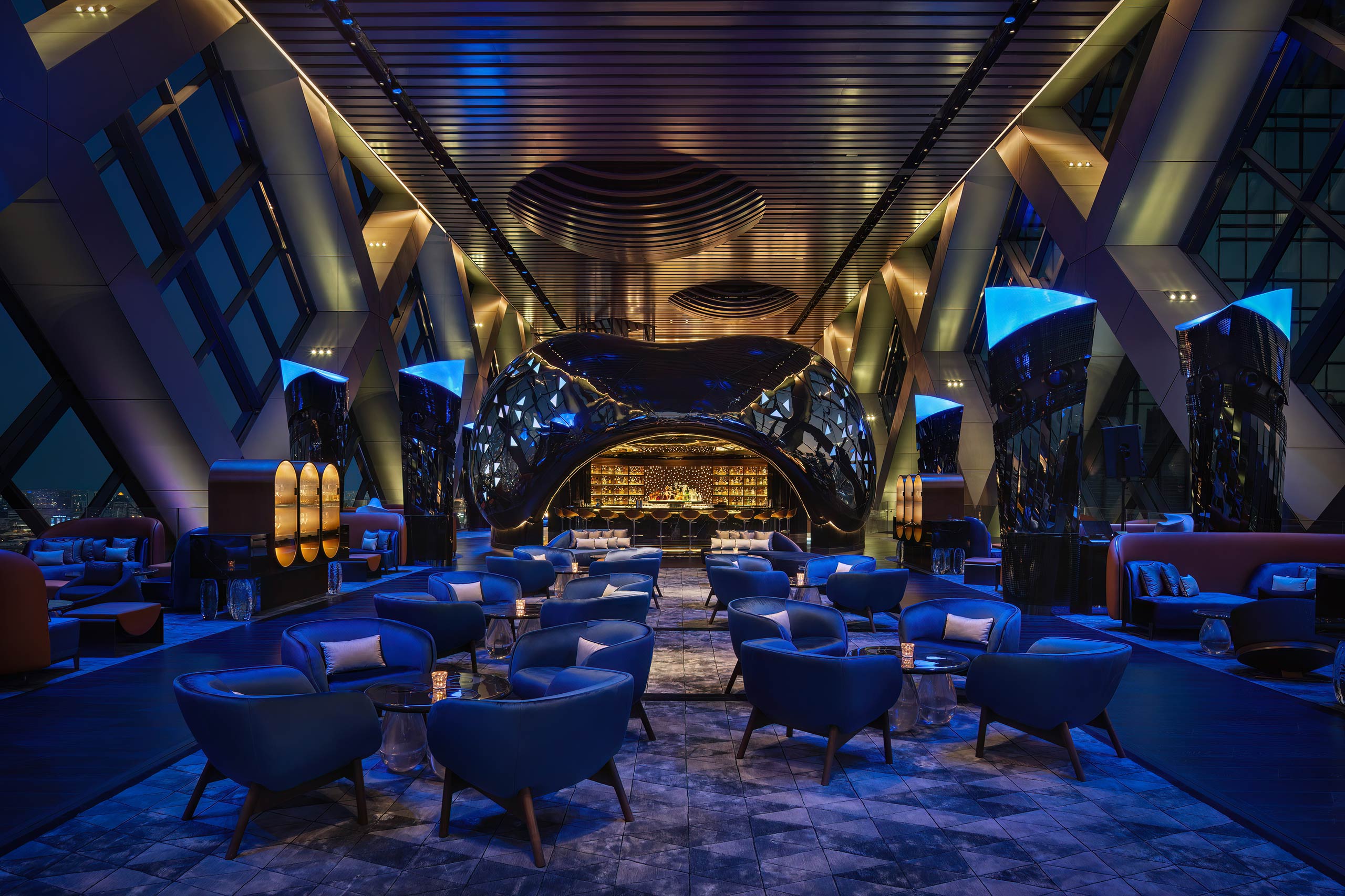 Luxurious bar lounge area with futuristic design, featuring blue-lit seating, modern architecture, and a sleek bar. The ambiance is elegant and inviting.